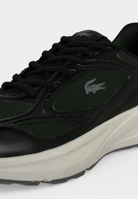 Baskets noires avec lacets noirs, semelle blanche et un logo crocodile gris sur le panneau latéral.