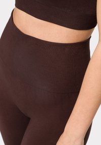 Brązowe sportowe legginsy z prążkowanego materiału, z wysokim stanem, gładką teksturą i dopasowanym krojem, podkreślające wygodę i elastyczność.