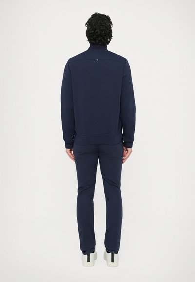 Tumesinine dressipluus kõrge krae, soonikkoes varrukasäärte ja sirge äärega, sobivate pükstega. Minimalistlik disain peene logoga.