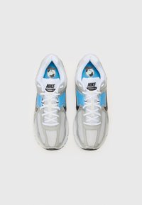 Nike Vomero 5 sportbačiai turi tinklelio ir sintetinį viršutinį sluoksnį, kuris yra pilkos ir mėlynos spalvos, su baltais raišteliais ir paminkštintu padu, suteikiančiu atramą.