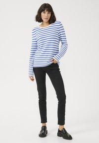 Chemise rayée bleu et blanc à manches longues avec un col rond, associée à un pantalon skinny noir et des mocassins noirs. Tissu texturé.