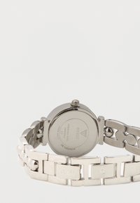 Zilveren horloge van roestvrij staal met een schakellint, voorzien van een ronde kast en een getextureerde achterkant met merkinscriptie. Geen zichtbaar wijzerplaat.