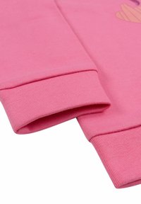 Cerniera della felpa rosa realizzata in materiale morbido. Texture a coste con orlo piegato, caratterizzata da dettagli di cucitura sottili.