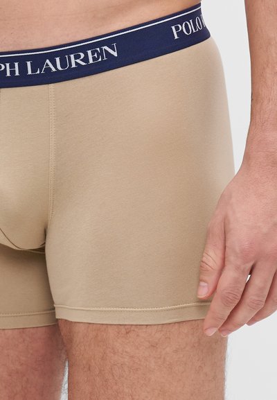 Beige bokserice iz mehkega bombaža. Temno modri pas z belim logotipom "POLO RALPH LAUREN". Gladka tekstura s prilagojeno zasnovo.