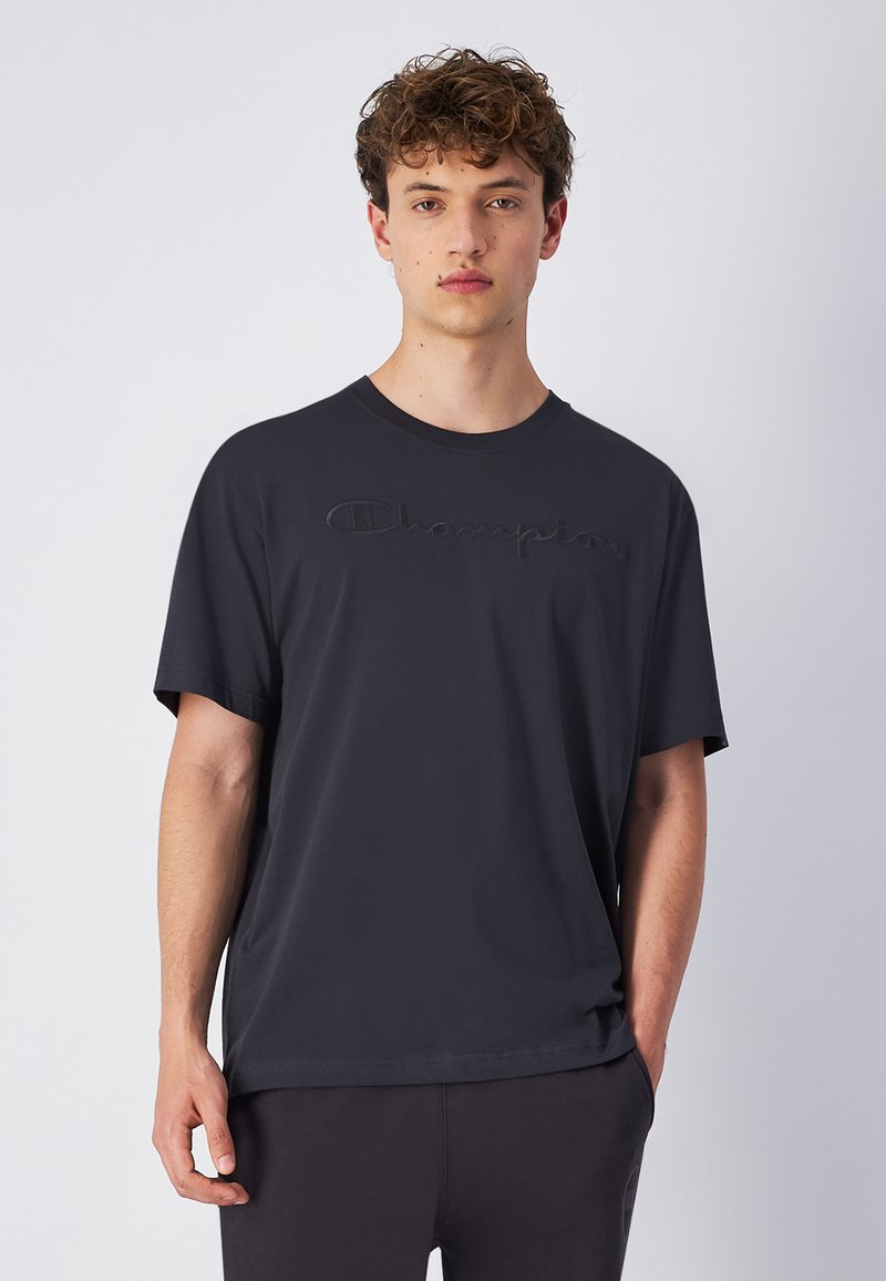 Sort bomulds t-shirt med korte ærmer, der har et hævet "Champion" logo tværs over brystet og en afslappet pasform. Glat tekstur og rund halsudskæring.