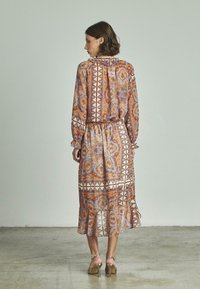 Robe à manches longues avec un motif dans des teintes orange et bleu, dotée d'une taille ceinturée, de poignets à volants et d'un ourlet évasé. Tissu lisse et léger.