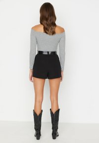Top gris de canalé con hombros descubiertos, pantalones cortos negros de talle alto y botas de vaquero negras hasta la rodilla. La tela suave y el diseño ajustado realzan la silueta.