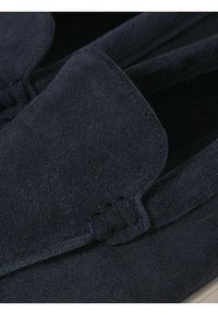 Gros plan sur un mocassin en daim bleu foncé avec des coutures visibles et une texture douce sur la partie supérieure de la chaussure.