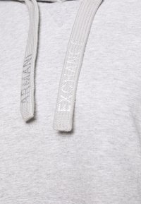 Szara bluza z kapturem z fakturowanej tkaniny, regulowanymi sznurkami w kapturze oraz napisem "Exchange" wydrukowanym w odblaskowym srebrze, o luźnym kroju.