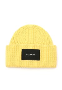 Gorro de punto amarillo con textura de canalé y un parche rectangular negro con texto blanco que dice "COACH."