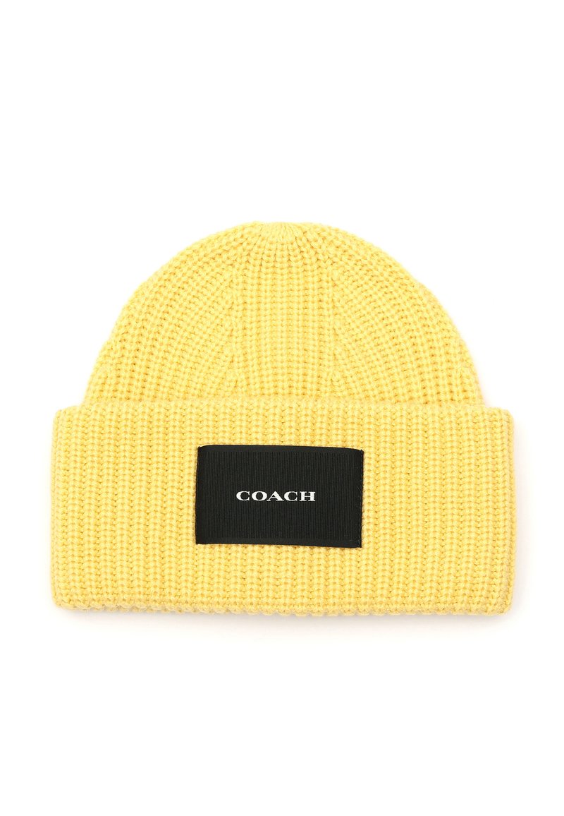 Gorro de punto amarillo con textura de canalé y un parche rectangular negro con texto blanco que dice "COACH."