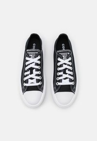 Zwarte canvas sneakers met witte veters en rubberen witte neuskap, met contrasterende stiksels en een logo op de tong.