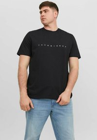 Zwart katoenen T-shirt met korte mouwen en ronde hals, voorzien van een wit "JACK & JONES" logo op de borst, gecombineerd met lichtblauwe spijkerbroek.