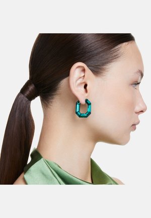 Teal geometric hoop earrings made of glossy material, featuring a hexagonal shape with angular facets, worn by a model with a ponytail.