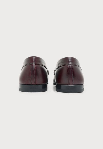 Paire de chaussures de ville en cuir marron foncé vues de dos, montrant les détails des coutures et des semelles noires sur fond blanc.