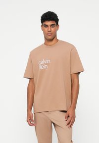 Rudas medvilninis marškinėliai su apvalia iškirpte ir trumpomis rankovėmis, priekyje vaizduojantis baltą "Calvin Klein" logotipą.