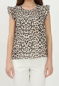 Blusa con stampa leopardata e maniche corte arricciate, in tessuto trasparente con macchie marroni e nere su sfondo chiaro, abbinata a pantaloni bianchi.