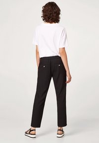 Pantaloni neri con vita elastica, vestibilità dritta e due tasche posteriori. Abbinati a una maglietta bianca e sandali neri.