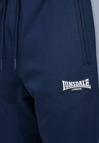 Navy blue athletic joggers made of soft fabric, featuring a Lonsdale London logo patch and an inset side detail in lighter gray.