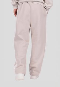 Világosszürke, laza szabású melegítőnadrágok fehér oldalsávokkal, elasztikus derékrésszel és szegélyekkel. Puha, texturált anyagból készültek.