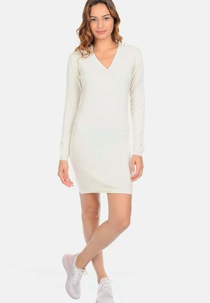 Robe à manches longues de couleur crème avec un décolleté en V et des détails de boutons. Design ajusté, longueur au genou, tissu texturé, associée à des baskets légères.