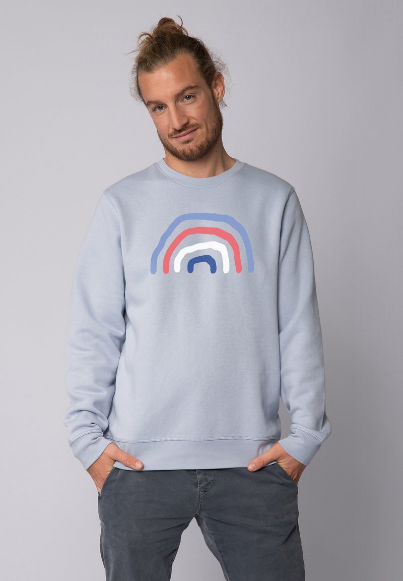 Lichtblauwe sweatshirt met een meerkleurige regenboogafbeelding in rood, wit en blauw over de borst. Gemaakt van zachte stof.