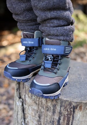 Hnedé a zelené nepremokavé topánky s čiernymi gumovými špičkami, modrými detailmi, šnurovacím zapínaním a polstrovanou členkovou oporou na drevenom povrchu.