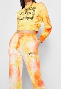 Geel en oranje tie-dye cropped sweatshirt met zwarte grafische print. Bijpassende tie-dye sweatpants met een kleine bedrukte afbeelding op het been.