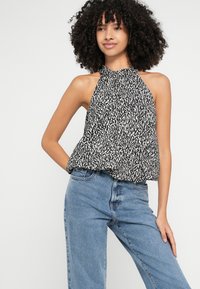 Melns un balts haltera top ar teksturētu, abstraktu rakstu, kombinēts ar gaisīgi zilām augsto jostasvietu džinsiem. Mīksta auduma un plūstoša piegriezuma.