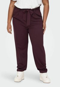 Burgundy tapered pants with a fabric belt, featuring side pockets and a smooth texture. Paired with white sneakers.