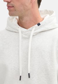 Sudadera gris clara con un acabado texturizado, que cuenta con una capucha con cordones, laces blancos con puntas negras y un pequeño logotipo en el pecho.