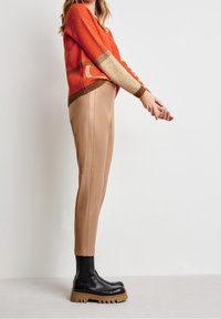 Orange och tan mönstrad stickad tröja, kombinerad med beige slim-fit byxor och svarta chunky ankelskids. Slät textur, avslappnad silhuett.