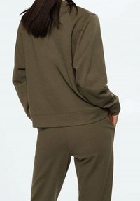 Sweatshirt vert olive, coupe décontractée, tissu texturé, poignets côtelés, bas assortis, poches latérales, design minimaliste.