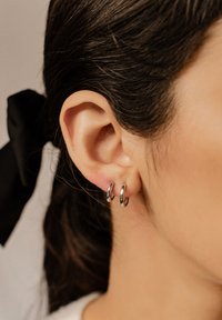 Orecchini a cerchio argentati esposti sull'orecchio di una donna, con una texture liscia e lucida e un design circolare semplice.