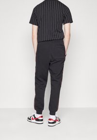 Černé pruhované tričko s krátkým rukávem doplněné černými zúženými jogger kalhotami, které mají červený boční pruh a elastické manžety. Bílá a červená obuv dotváří celý vzhled.