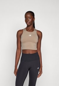 Beige avskåret tanktopp med hvit logo, kombinert med høyt liv svarte leggings. Begge plaggene har en elegant, figurnær design.