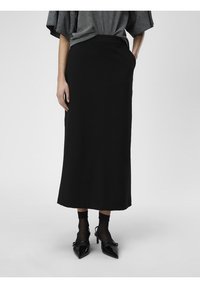 Schwarzer Midirock mit taillierter Passform, glatter Textur, ohne sichtbare Muster, kombiniert mit schwarzen spitzen High Heels und durchsichtigen schwarzen Socken.