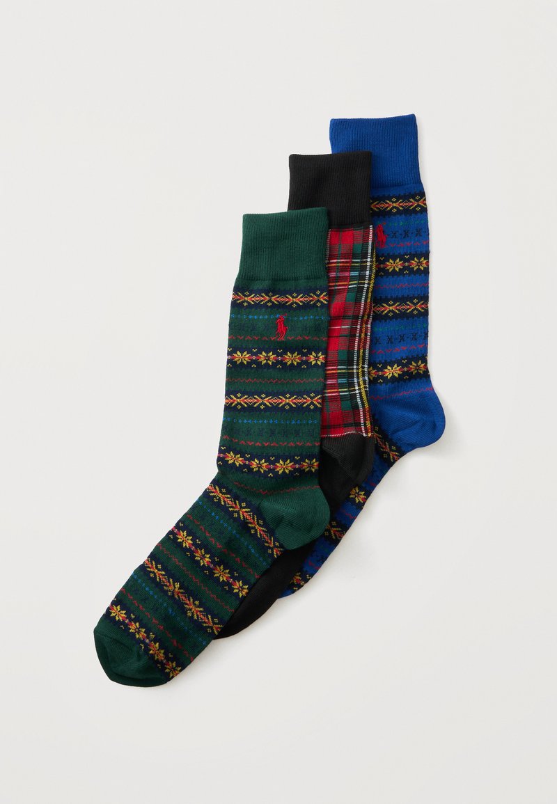 Trois chaussettes montantes colorées avec des motifs verts, écossais rouges et bleus, superposées sur un fond blanc.