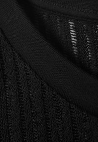 Tissu en tricot noir avec une texture côtelée et un col noir uni et lisse. Le matériau présente des sections à tissage ouvert pour la respirabilité.