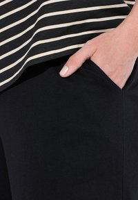 Pantalones de tela negra con un bolsillo visible, combinados con una blusa que presenta rayas horizontales en color beige. Textura suave, diseño casual.