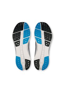 Zapatos deportivos grises con una media suela blanca, que presentan un patrón texturizado, suela de goma negra y azul con agujeros de ventilación y almohadillas de tracción.