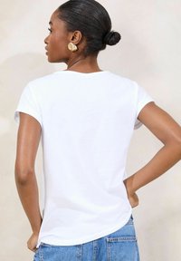 T-shirt bianca in cotone con maniche corte arrotolate, scollatura rotonda e orlo arrotondato, abbinata a jeans blu in denim.