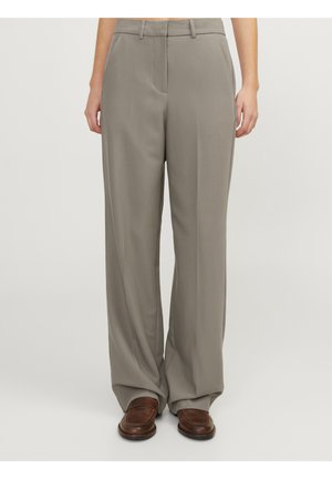 Pantalon droit taupe avec poches avant, porté avec des mocassins en cuir marron sur une personne debout devant un fond uni.