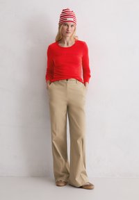 Rotes Langarmshirt mit "Marc O'Polo"-Schriftzug, beigen weit geschnittenen Hosen und einer rot gestreiften Mütze. Weiche Texturen und lässige Passform.