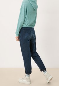 Felpa con cappuccio tessuta in teal chiaro, abbinata a jeans tapered blu scuro. Sneakers bianche con suola spessa e orli arrotolati sui jeans.