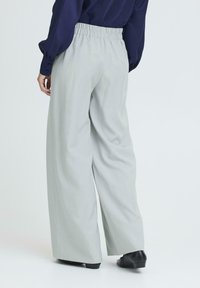 Šviesiai pilkos plačios kelnės iš audinio, turinčios elastinę juosmenį. Lygus tekstūras, minimalistiškas dizainas, derinamas su juodais bateliais.