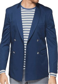 Granatowa, dwurzędowa marynarka o dopasowanym kroju, z jedną kieszenią na piersi i srebrzystymi guzikami, noszona z pasiastą niebiesko-białą koszulą pod spodem.
