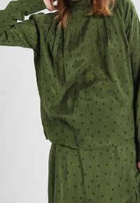 Blouse verte et jupe assortie en tissu doux, présentant une coupe décontractée, un motif en losanges et des détails froncés au niveau de l'encolure.