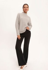 Jasnoszara sweter z dzianiny o splocie kablowym, z wysokim kołnierzem, zestawiony z czarnymi dopasowanymi spodniami i kremowymi butami typu slip-on. Gładka tekstura i luźny krój.