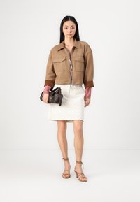 Bruine cropped jacket met twee borstzakken, gedragen over een rood-wit geruit shirt. Witte knie-lange rok met subtiele diagonale lijnen.